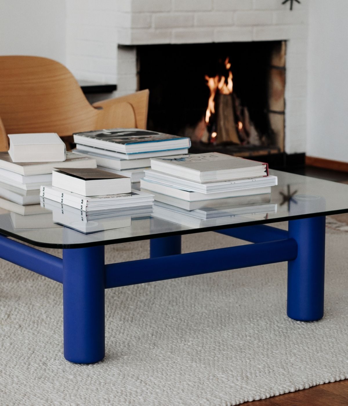 Boundary Couchtisch in Blau von Massproductions, im Wohnzimmer platziert und mit Büchern dekoriert. Die klare geometrische Form des Tisches und die elegante blaue Oberfläche ergänzen das moderne Interieur, während die Bücher eine gemütliche und einladende Atmosphäre schaffen..
