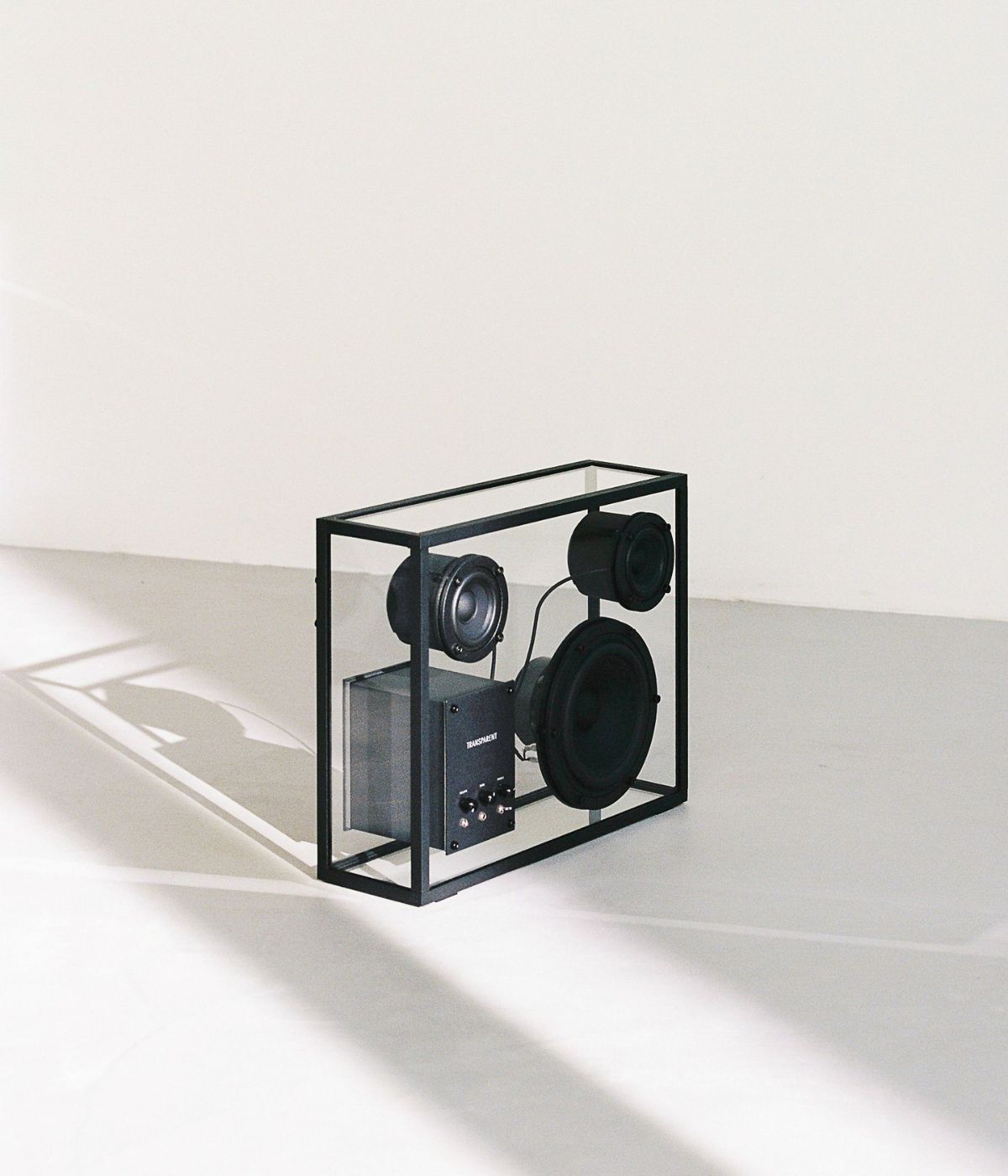 Large Speaker leicht seitlich aufgenommen, mit Sonnenlicht und Schatten auf dem Boden. Das weiche Licht betont die Form des Lautsprechers und schafft eine warme, einladende Atmosphäre im Raum.“