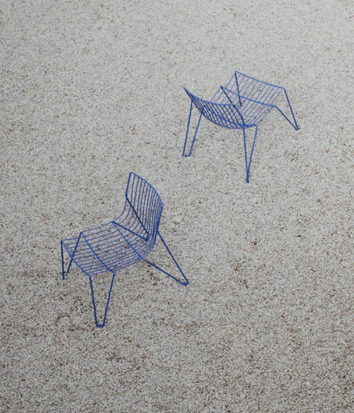 Zwei TIO Easy Chairs in sanftem Blau von Massproductions, aus der Vogelperspektive auf hellem Kiesboden inszeniert – minimalistische Stühle mit klarer Linienführung, die ein modernes Design im harmonischen Zusammenspiel mit der natürlichen Kiesumgebung präsentieren
