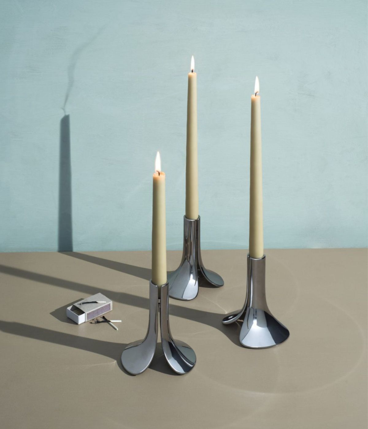 Drei Pinci Kerzenständer von Massproductions aus Zamak mit integrierter Scharnierkonstruktion, die Kerzen selbsttätig fixiert, vor weißem Hintergrund – minimalistisches, funktionales Design.