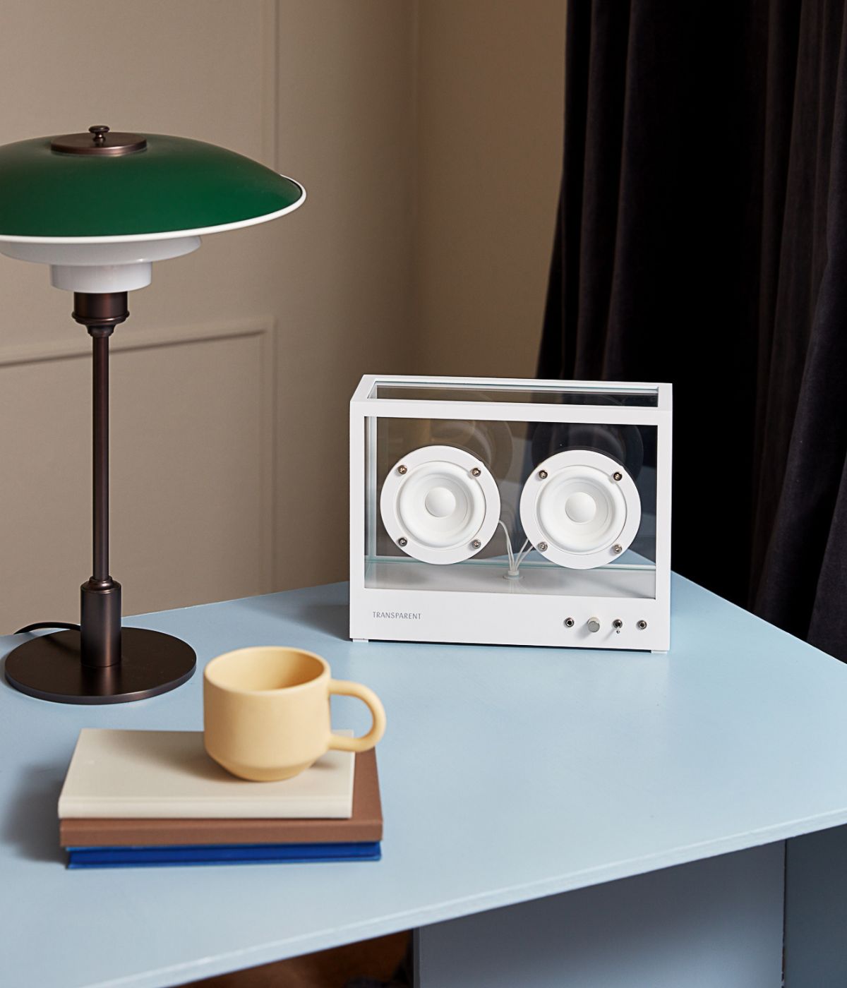 Small Transparent Speaker in Weiß auf einem blauen Schreibtisch. Der Lautsprecher hebt sich mit seinem minimalistischen Design vom kräftigen Blauton des Tisches ab und passt perfekt in ein modernes Arbeitsumfeld.
