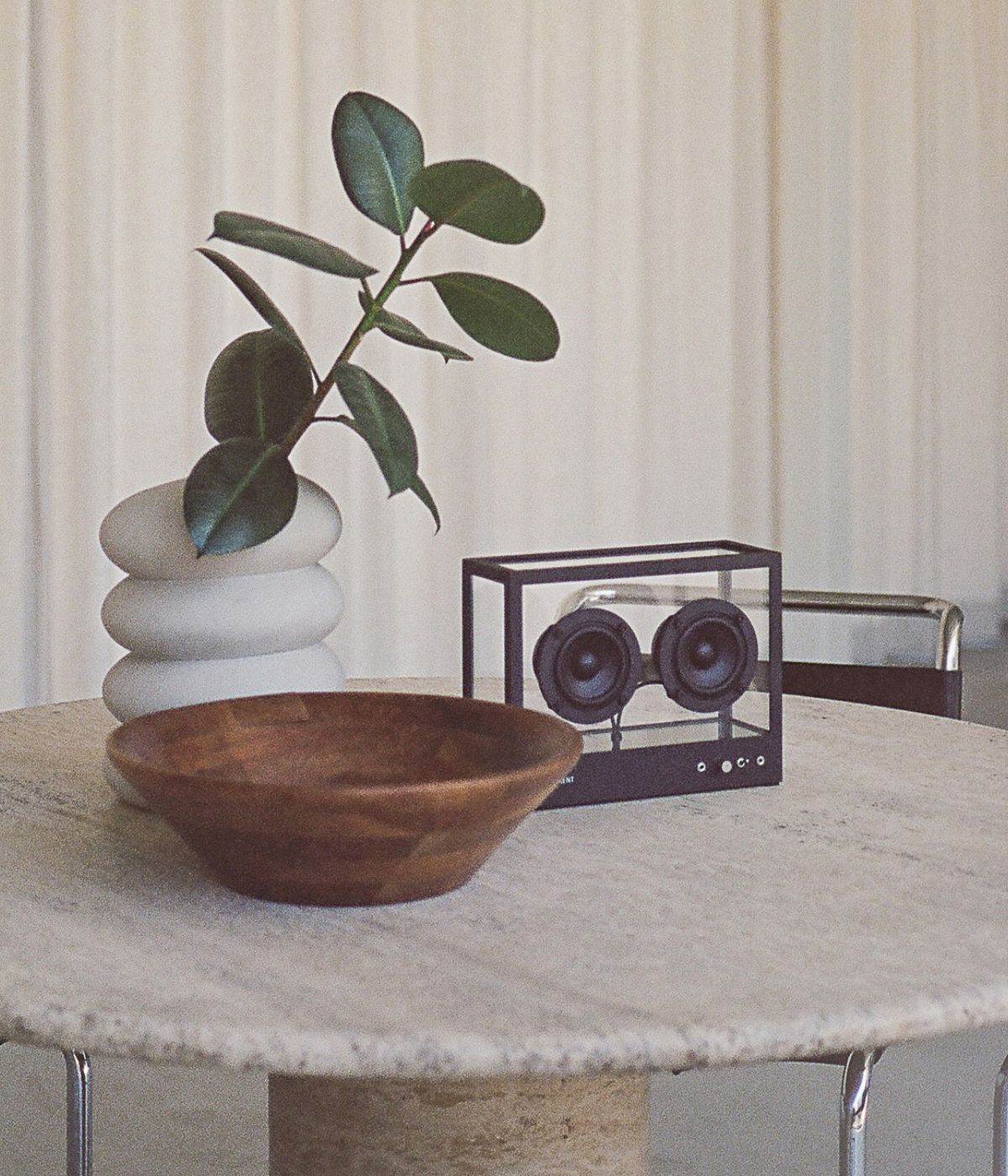 Small Transparent Speaker inszeniert auf einem edlen Tisch. Der Lautsprecher mit seinem transparenten Gehäuse und minimalistischen Design steht prominent im Vordergrund auf einer hochwertigen Tischplatte aus dunklem Holz oder edlem Material. Im Hintergrund deuten unscharfe Elemente auf ein stilvolles Wohn- oder Arbeitsumfeld hin, was die elegante und moderne Wirkung des Lautsprechers unterstreicht. Die klare Struktur des Speakers harmoniert mit der edlen Oberfläche des Tisches und schafft eine ruhige, desig