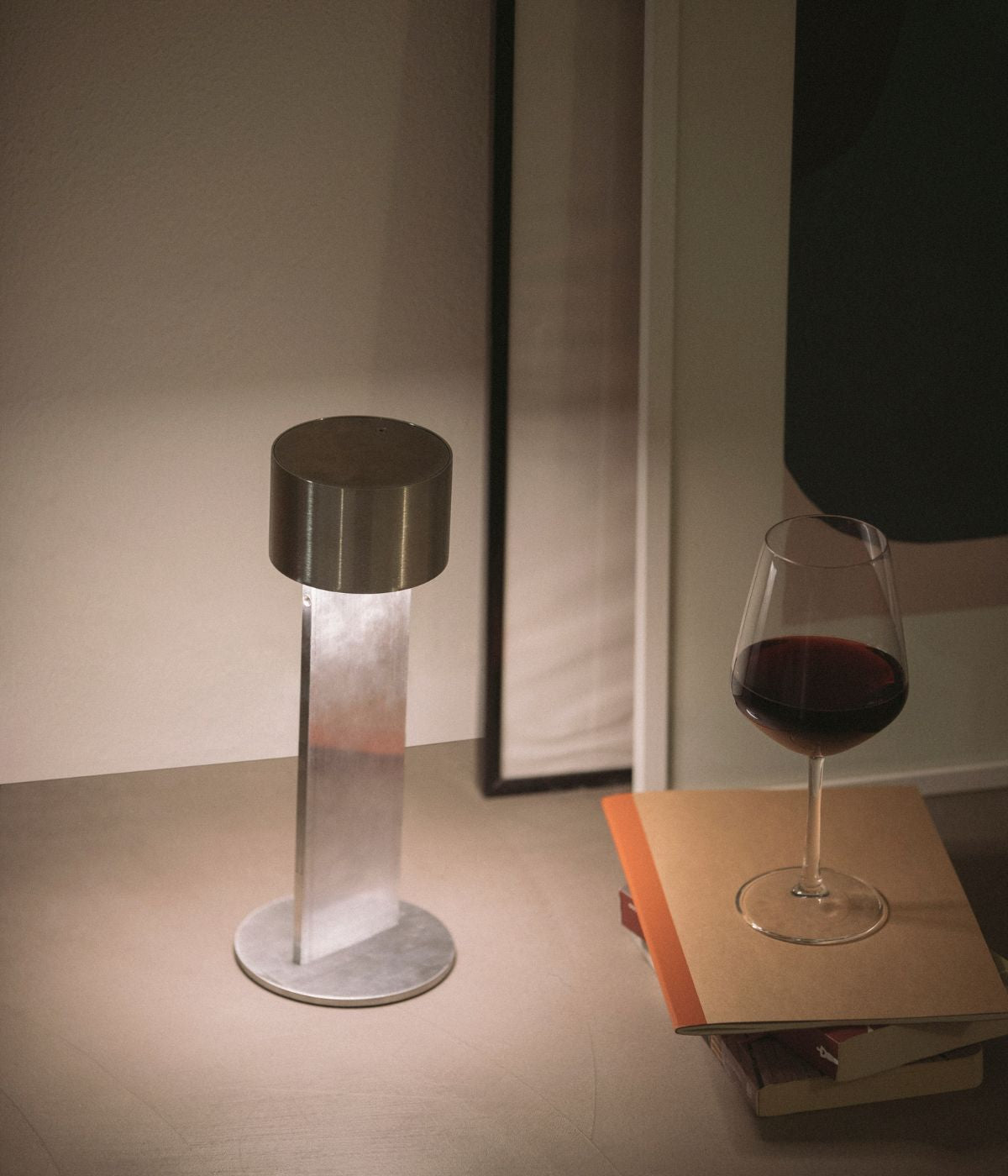 Akkubetriebene Times Leuchte in unbehandelter Raw-Metalloptik von From Lighting, dekorativ auf einem Holztisch neben einem halb gefüllten Weinglas arrangiert – stilvolle Kombination aus Industrial-Design und gemütlicher Atmosphäre
