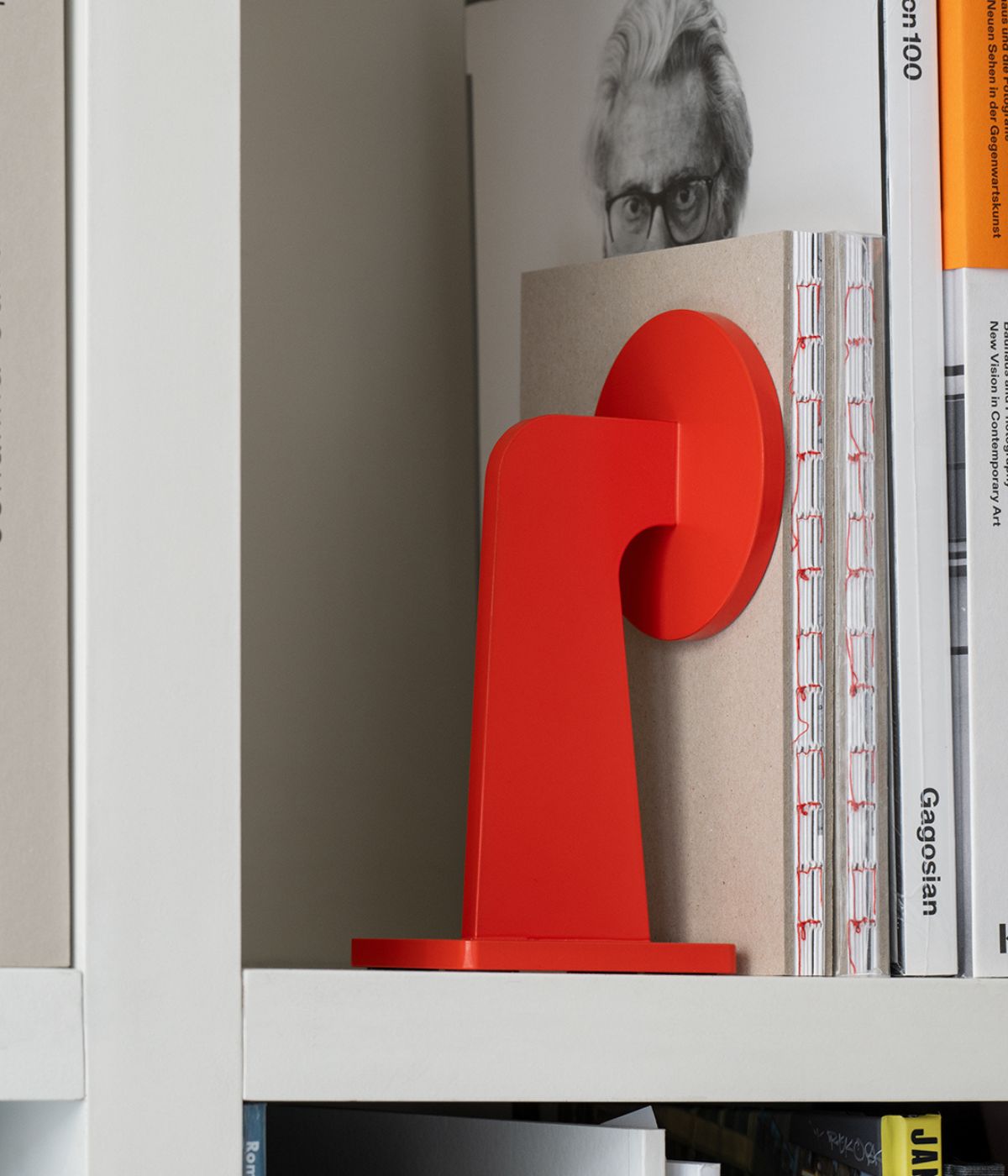 Massproductions BUFFER Buchstütze in kräftigem Rot, aus pulverbeschichtetem Metall gefertigt und dekorativ mit aufgestellten Büchern inszeniert – markantes, funktionales Accessoire für Regal oder Tisch  
